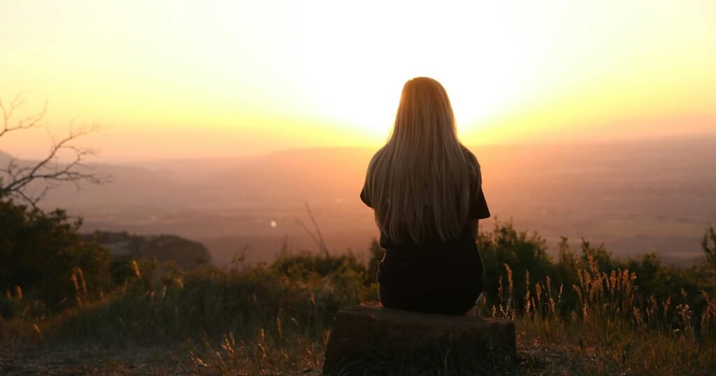 Woman showing signs she is disconnected from her body, sitting alone at sunset.